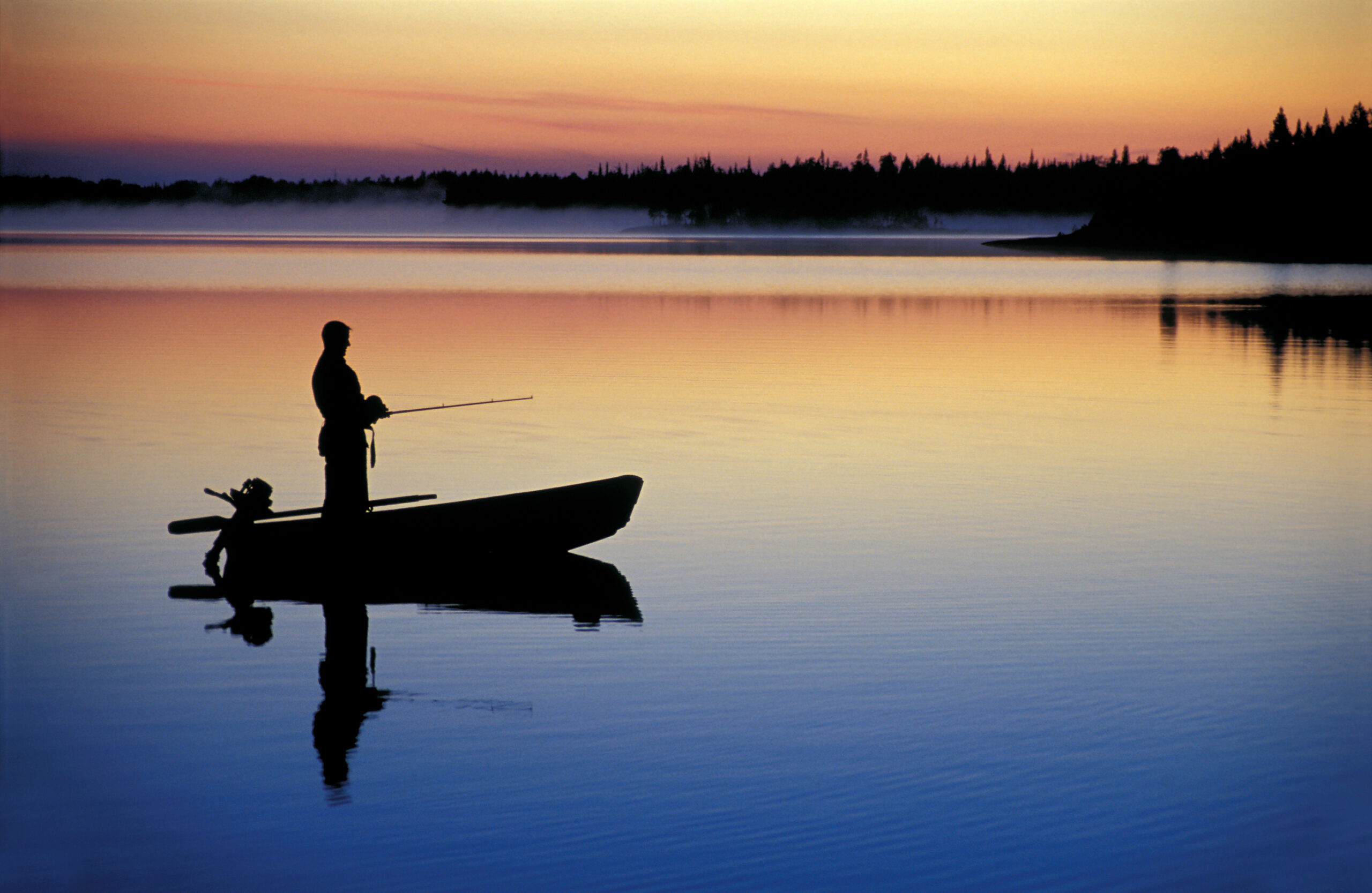 Fisherman's silouette against a breathtaking sunset on the lake in a boat