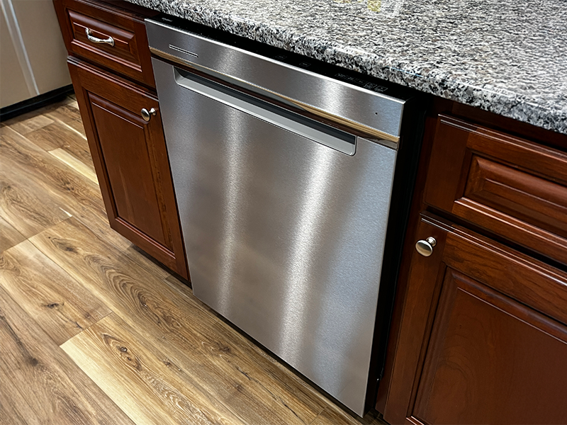 dishwasher Stainless steel dishwasher in between two wooden cabinet doors under a countertop.