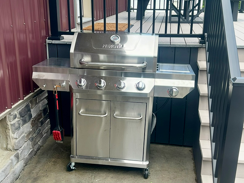 Silver steel gas grill in corner of a black barred gate