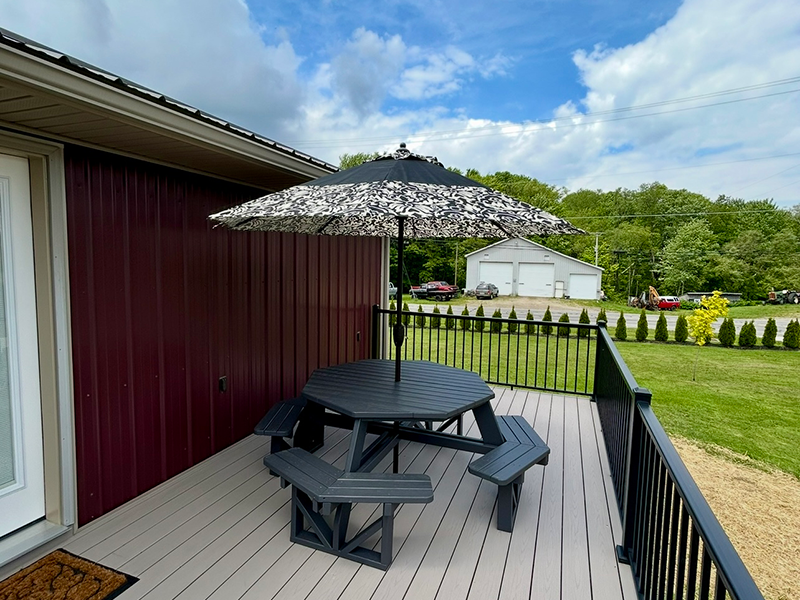 patio Black circular patio table with grey umbrella on a wooden deck outside of the Pymatuning Lake Lodge