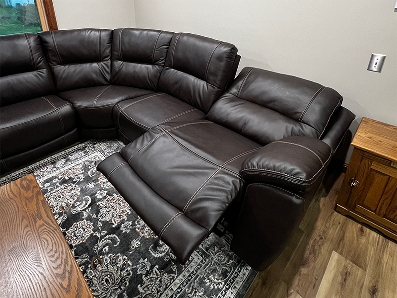 recliner Brown leather arm couch sitting atop a woven rug on a wooden floor in a living room.